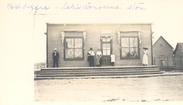 Gens devant le bureau de poste (puis Donovan’s Store) et gens devant la maison Ramsay à Maniwaki, décorée avec des drapeaux